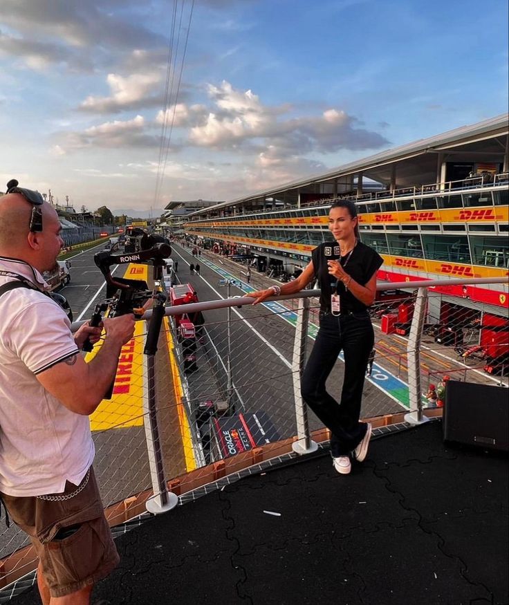 a man holding a camera next to a woman on top of a race track in front of a crowd