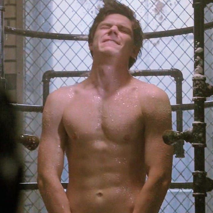 a shirtless man standing in front of a metal cage with water droplets on it