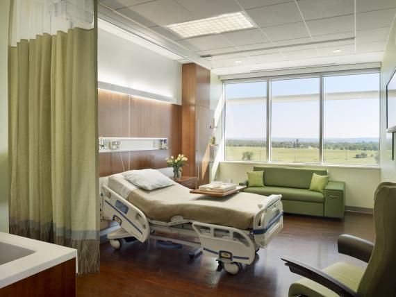 a hospital room with a bed, couch and window overlooking the field in front of it