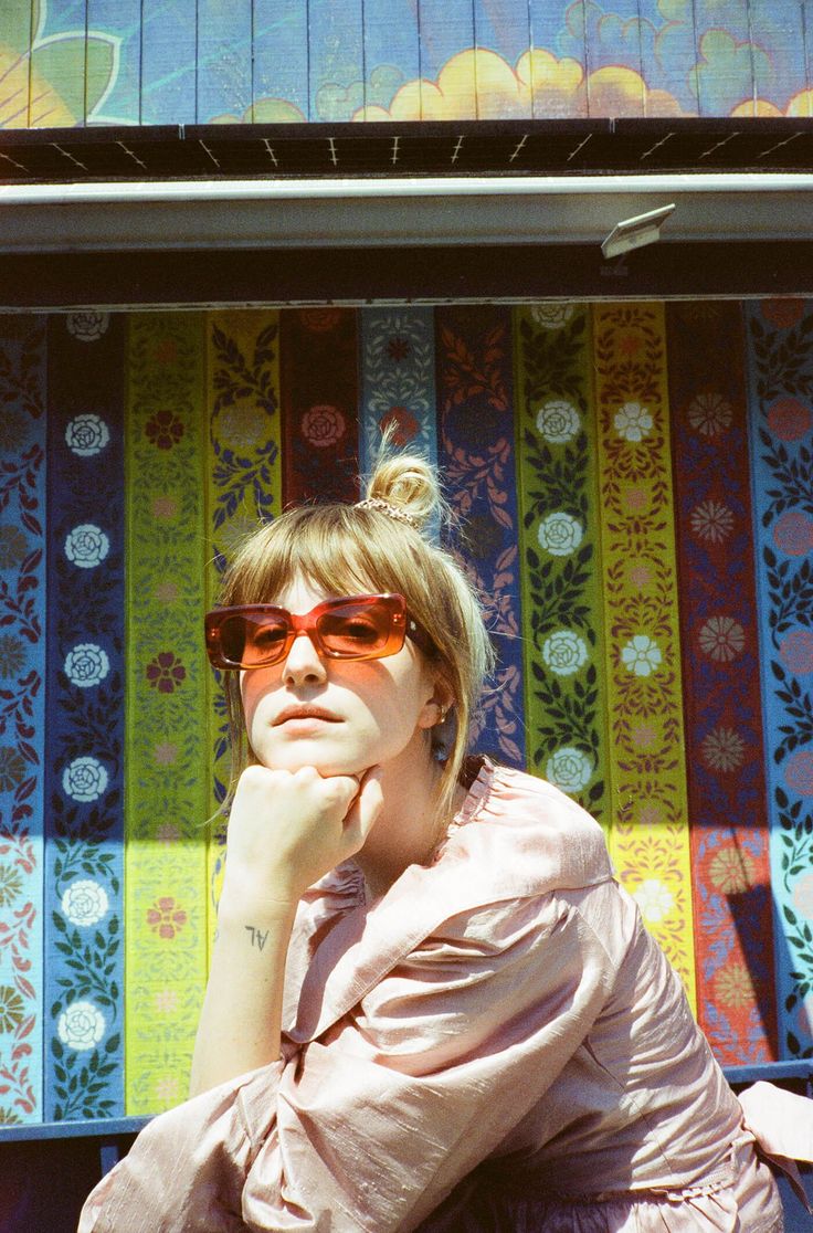 a woman wearing sunglasses sitting in front of a colorful wall