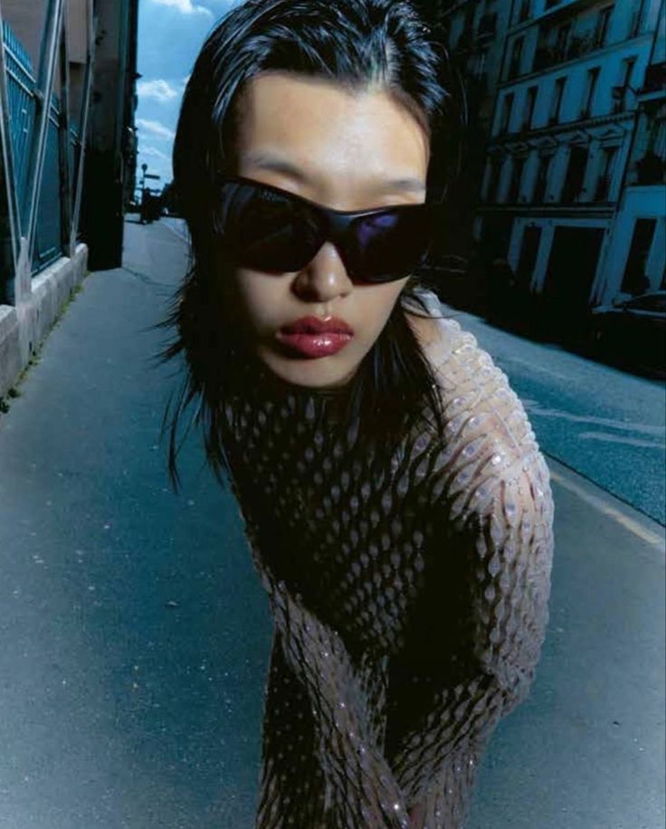 a woman with sunglasses on walking down the street in front of some buildings and looking at the camera