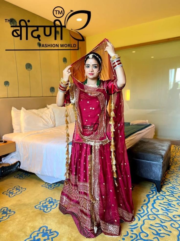 a woman in a red dress is standing near a bed and holding her hands up to her head