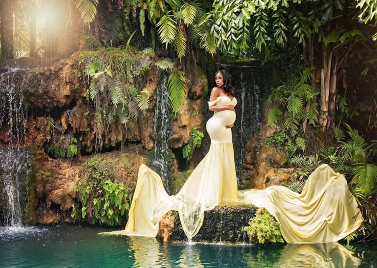 a woman in a yellow dress standing next to a pool with waterfalls and greenery