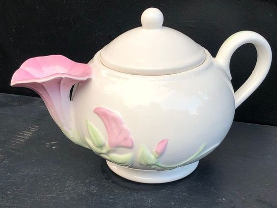 a white tea pot with pink flowers painted on the outside and inside, sitting on a black surface