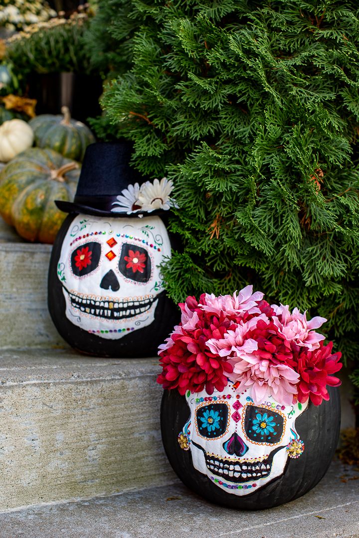 two decorated pumpkins sitting on the steps with flowers in their heads and one has a skull face painted on it