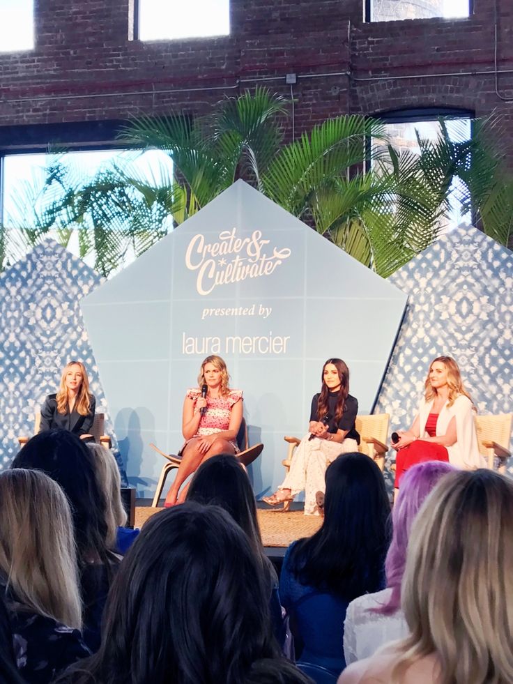 three women are sitting on stage talking to each other in front of a large group of people