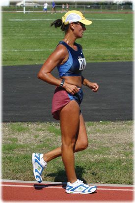 a woman running on a track in a blue top and maroon skirt with white sneakers