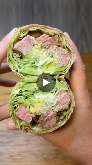 a person holding up a sandwich with meat and lettuce in the wrapper