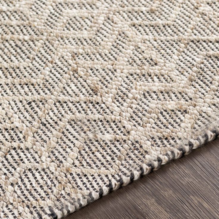 a close up view of a rug on a wooden floor with the area rug in grey and white