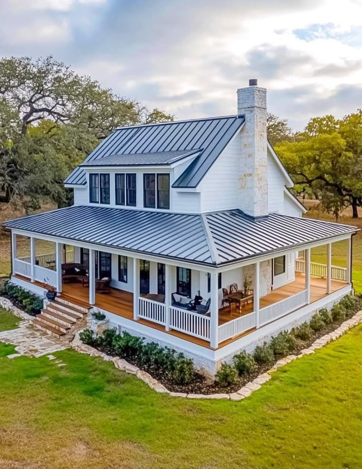 a large white house with a metal roof and covered porch in the middle of an open field