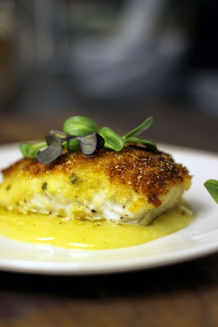 a white plate topped with fish covered in sauce and green garnish on top of a wooden table