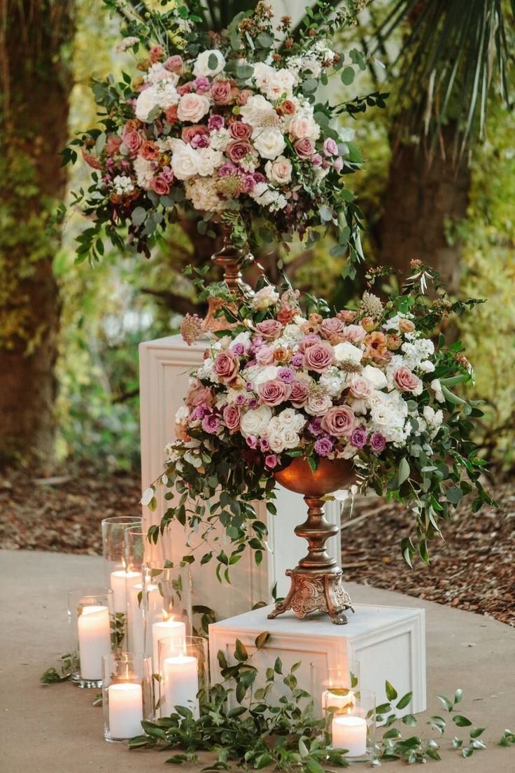 an arrangement of flowers and candles on a pedestal