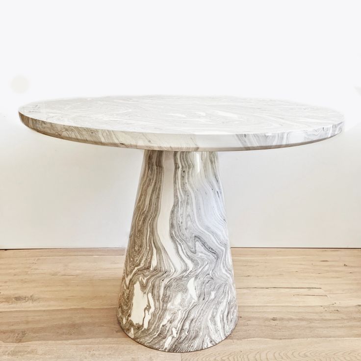 a round marble table on wooden flooring with white wall in the backround