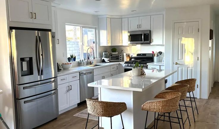 a kitchen with white cabinets, stainless steel appliances and wicker bar stools in front of the island