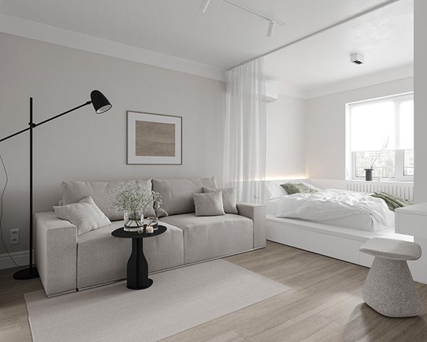 a living room with white walls and wood floors is pictured in this image, there is a large bed next to the couch