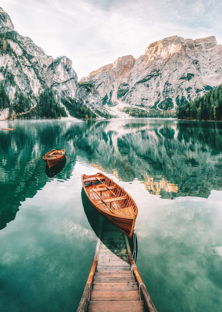 two small boats are docked at the end of a pier in front of some mountains