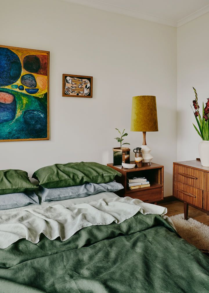 a bed with green sheets and pillows next to a painting on the wall above it