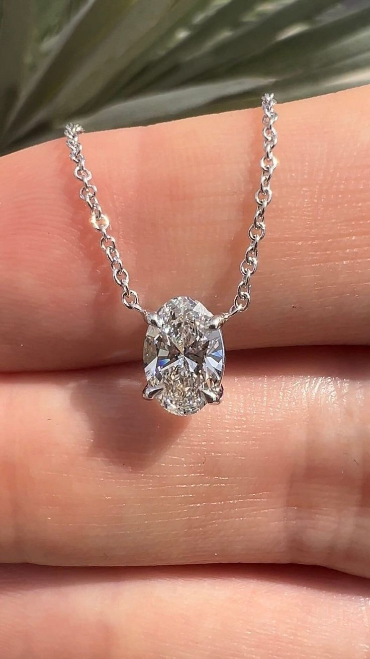 a woman's hand holding a diamond necklace on her left side, with a plant in the background