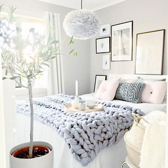 a bedroom with white walls and pictures hanging on the wall above the bed, next to a potted plant