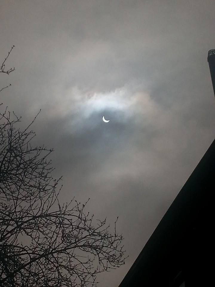 the sun is shining brightly in the cloudy sky over some buildings and trees with no leaves on them