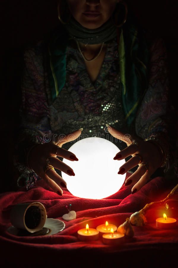 a woman is holding out her hands over a glowing orb in the dark with candles around it