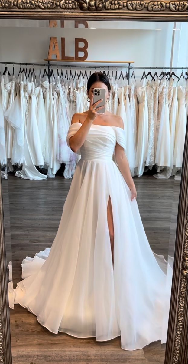 a woman taking a selfie in front of a mirror wearing a white wedding dress