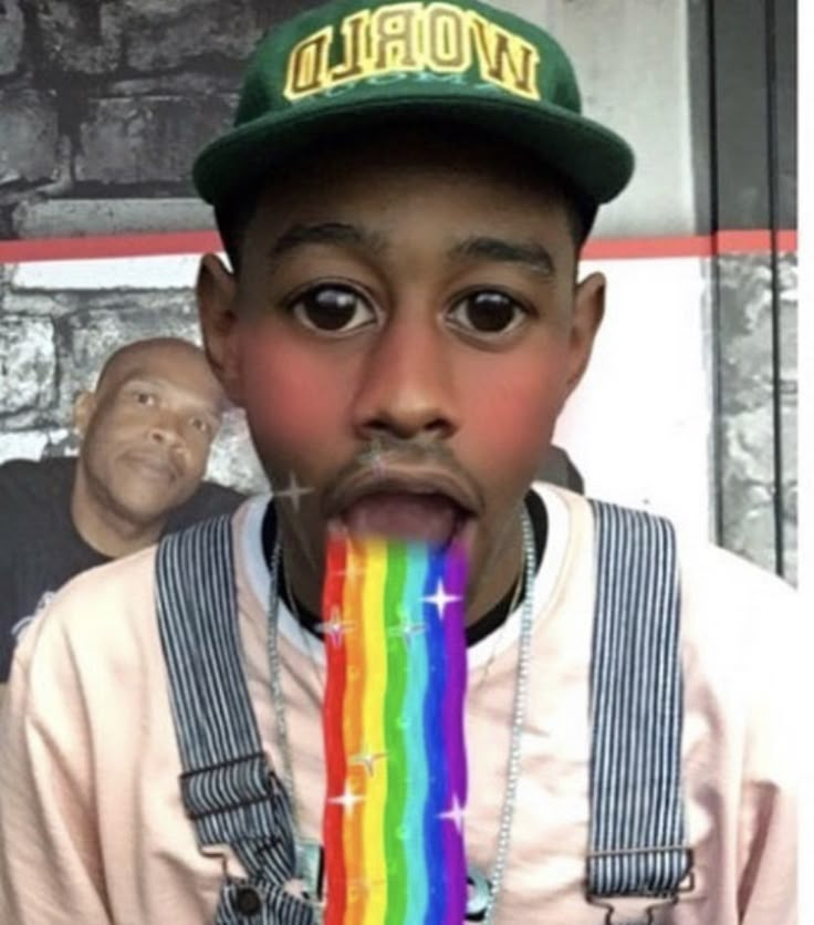 a young boy wearing suspenders and a green hat eating a rainbow lollipop