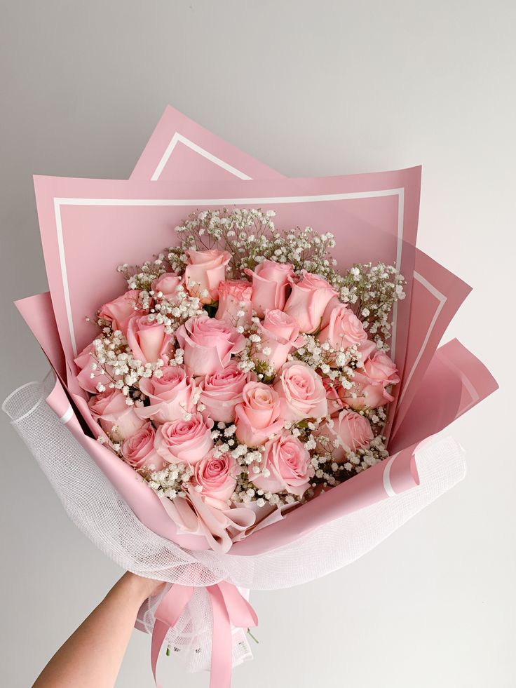 pink roses and baby's breath are in a paper bouquet for someone to hold