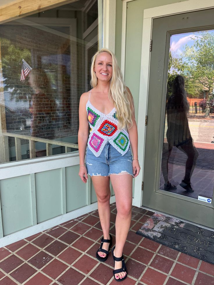 a woman standing in front of a building wearing shorts and a crochet top