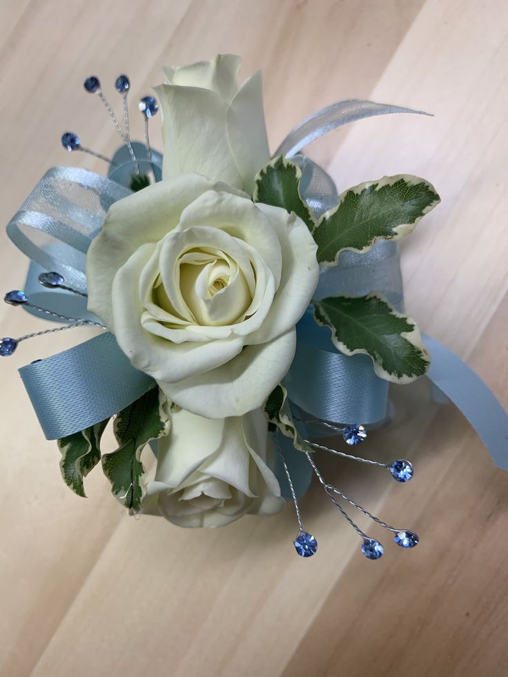 a white rose and blue ribbon bouquet on a wooden table with silver pins in the center