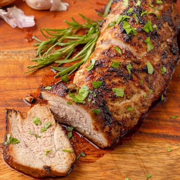 a piece of meat on a cutting board next to garlic and green onions with some seasoning