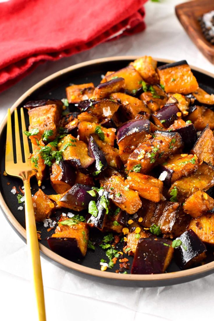 a black plate topped with cooked eggplant next to a fork