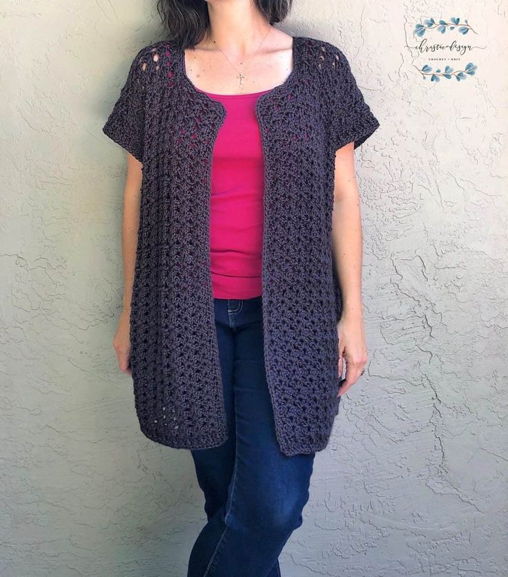 a woman standing in front of a white wall wearing a purple top and black cardigan