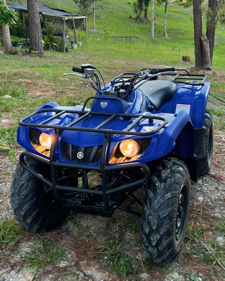 a blue four - wheeler parked in the woods with its lights turned on and it's front tire missing