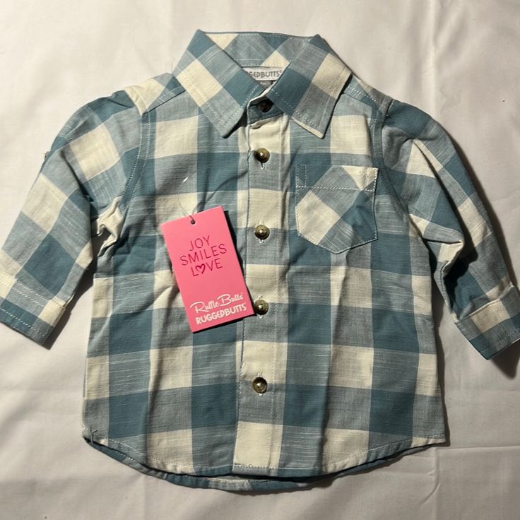 This New With Tags, Button Down Shirt Size 3-6 Months Is Adorable With A Blue And White Checkered Pattern, Buttons At The Elbows To Roll Up The Sleeves, And A Pleated Back. Ruggedbutts Is An Excellent Quality Clothing. Cute Blue Button-up Shirt, Blue Long Sleeve Shirt For Playtime, Cute Blue Collared Shirt, Cotton Button-up Tops For Playtime, Collared Tops With Buttons For Playtime, Cotton Tops With Button Closure For Playtime, Blue Shirt With Buttons For Playtime, Blue Button-up Tops For Playtime, Blue Shirt For Playtime