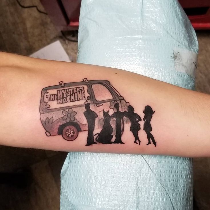 a small tattoo on the arm of a woman with people and a van behind her