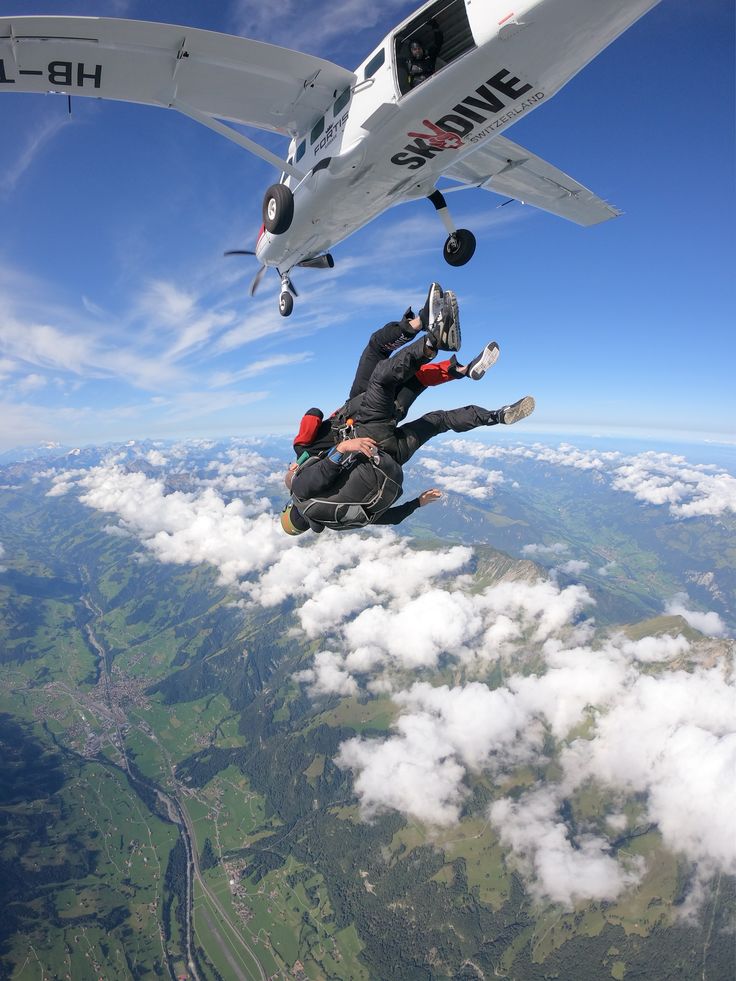 two people are in the air with an airplane above them and one person is upside down