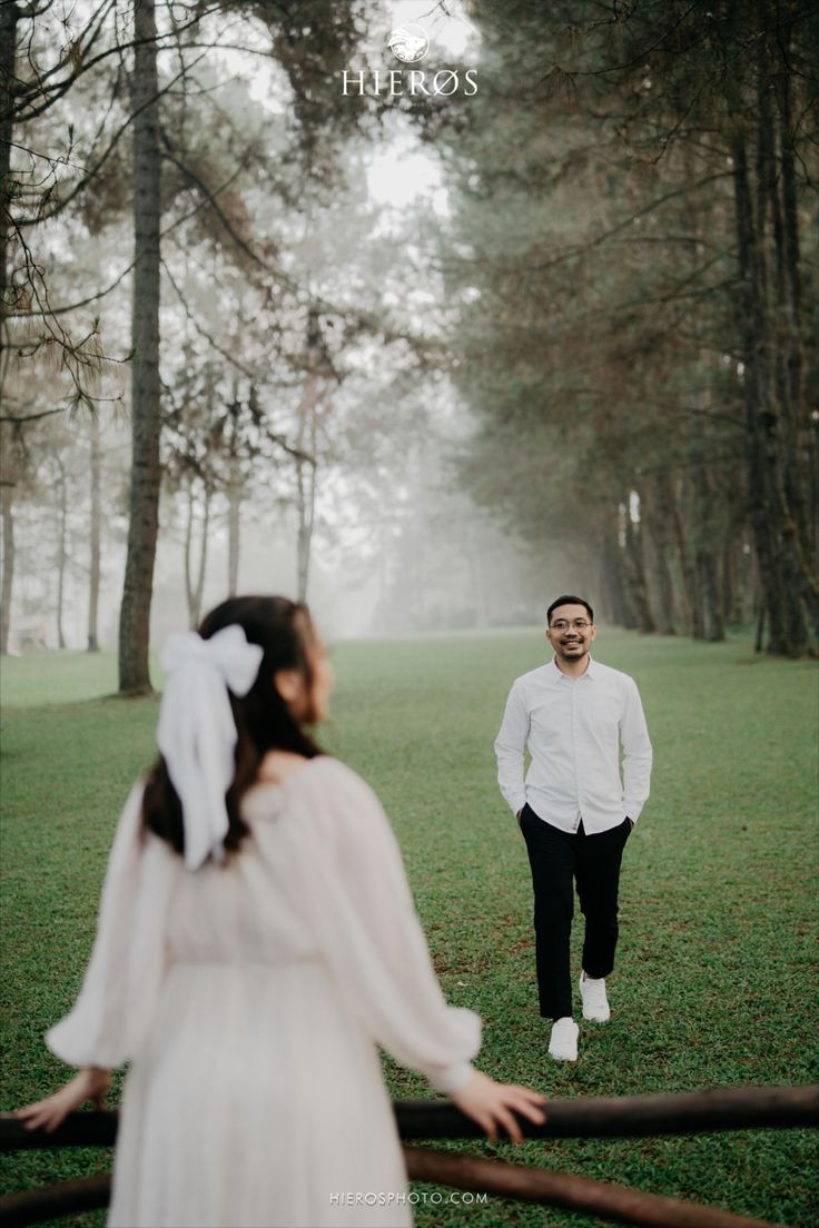 a man standing next to a woman in a white dress on top of a lush green field