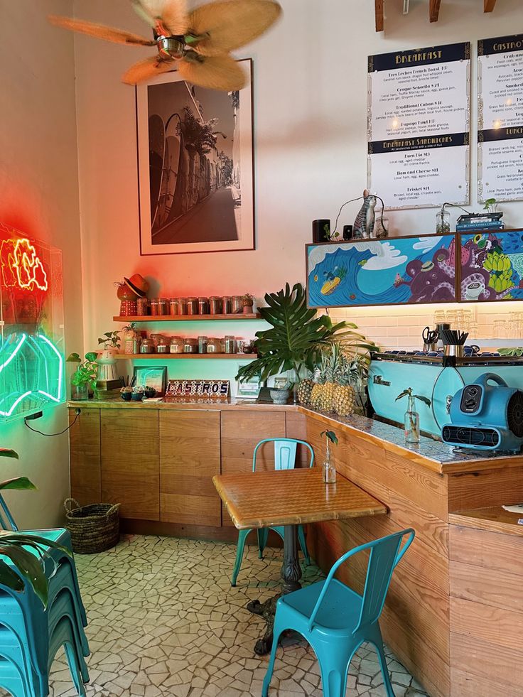 the inside of a restaurant with blue chairs and neon signs on the wall above it