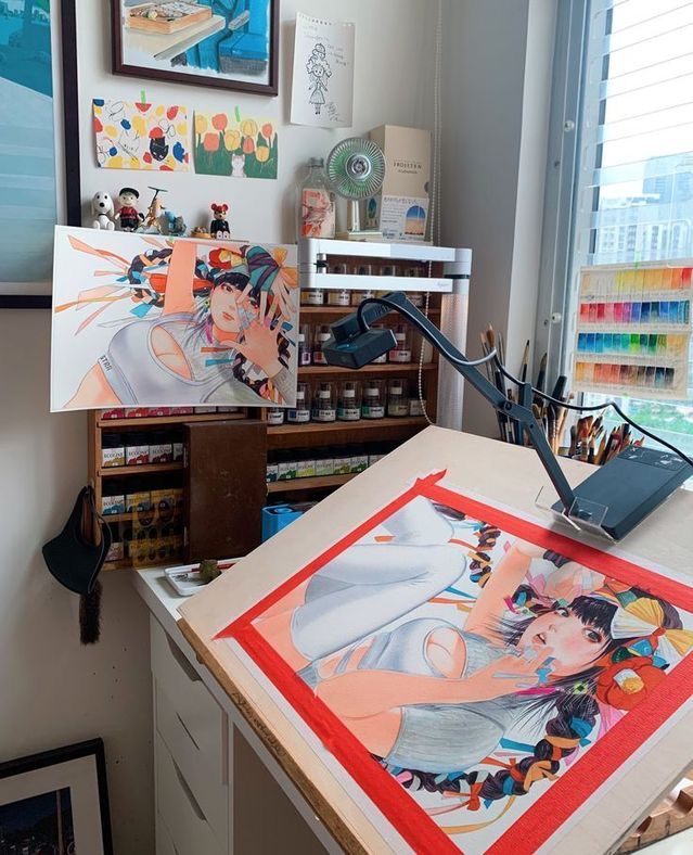 an artist's studio with art supplies on the table and paintings hanging up in front of it