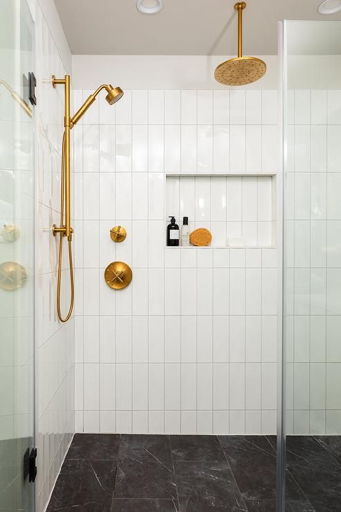 a white tiled bathroom with gold fixtures and black floor tiles on the shower wall, along with two brass faucets