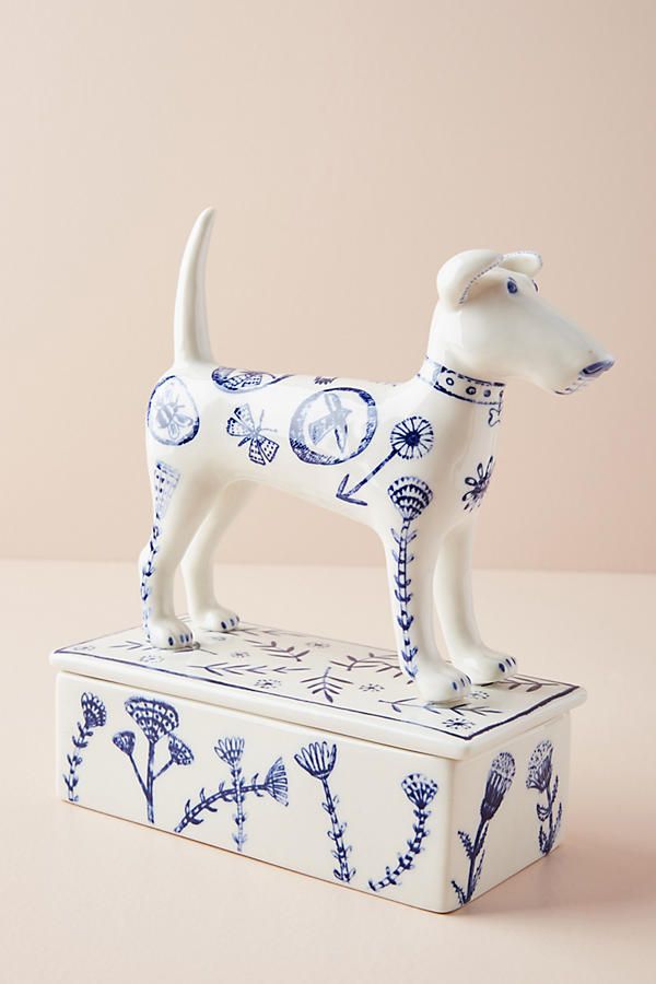 a white dog figurine sitting on top of a blue and white tin box