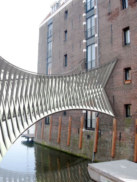 a bridge that is over some water in front of a brick building with windows on each side