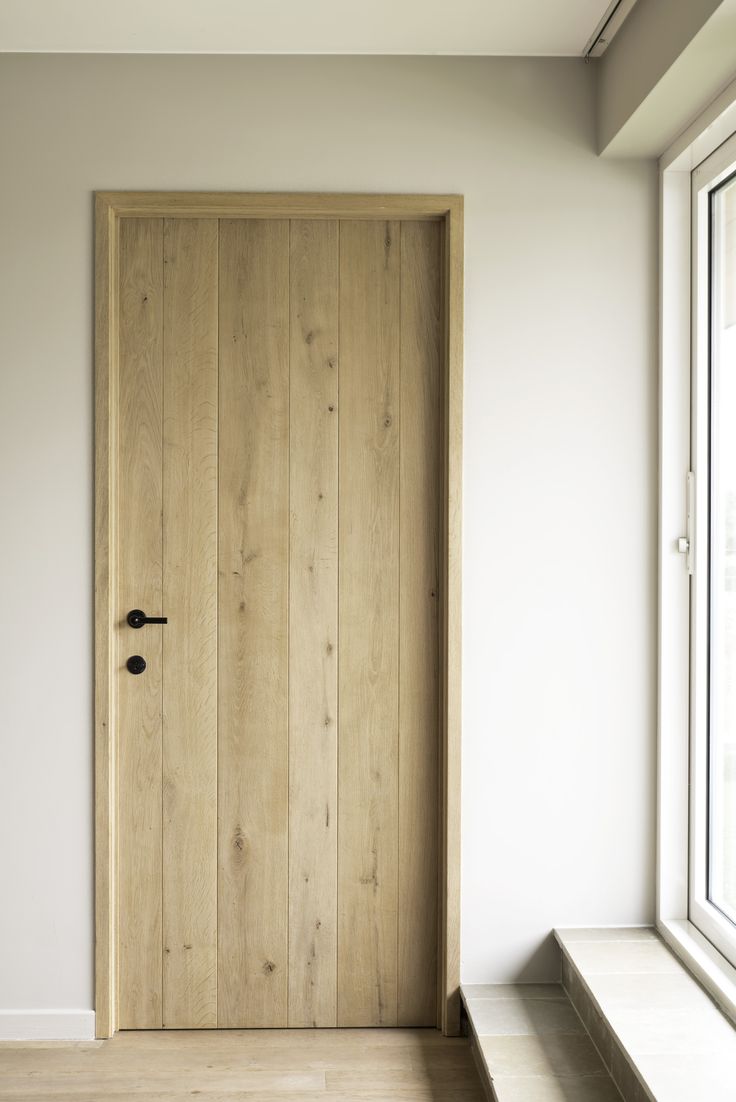 a wooden door sitting next to a window in a white walled room with wood flooring