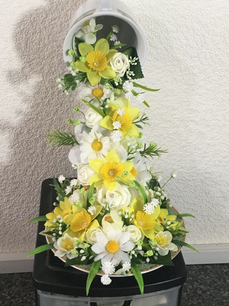 a bunch of flowers sitting on top of a black trash can in front of a white wall