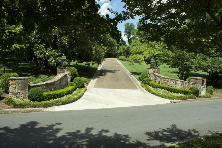 an entrance to a driveway surrounded by lush green trees