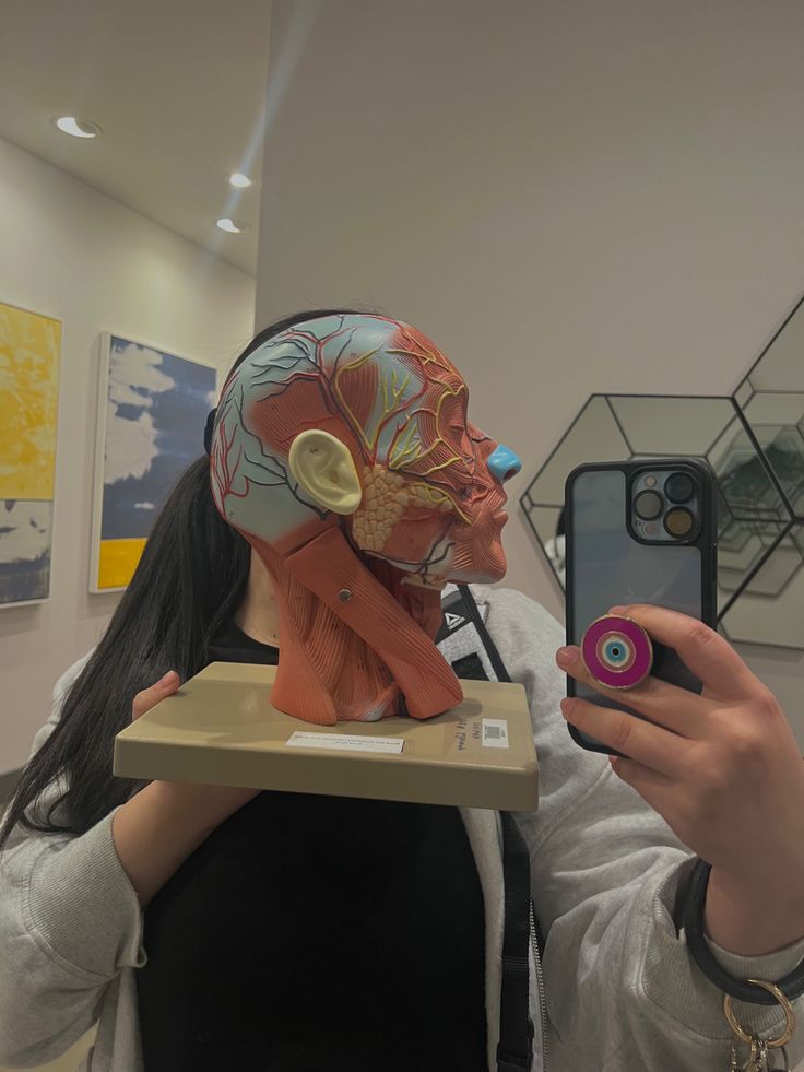 a woman taking a selfie with her cell phone while wearing a human head mask