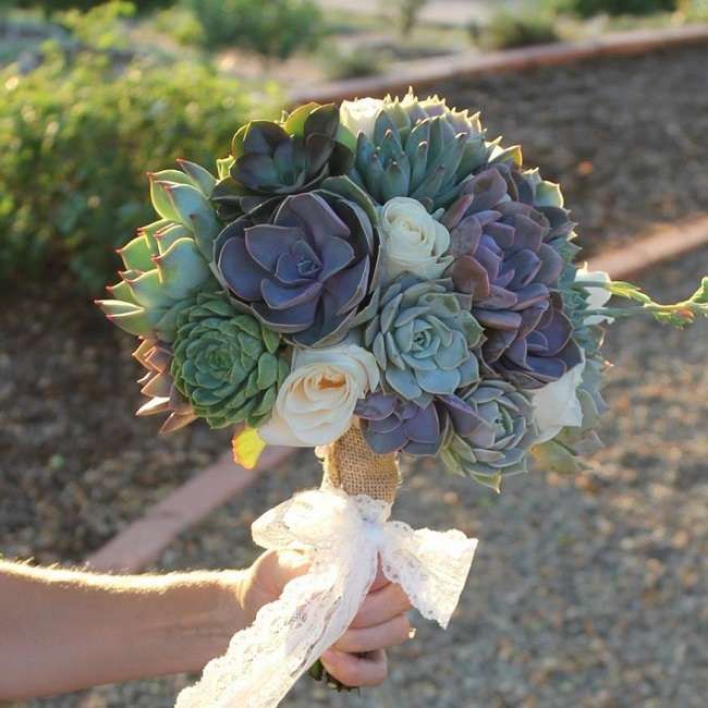 a bride's bouquet with succulents and roses is held in her hand