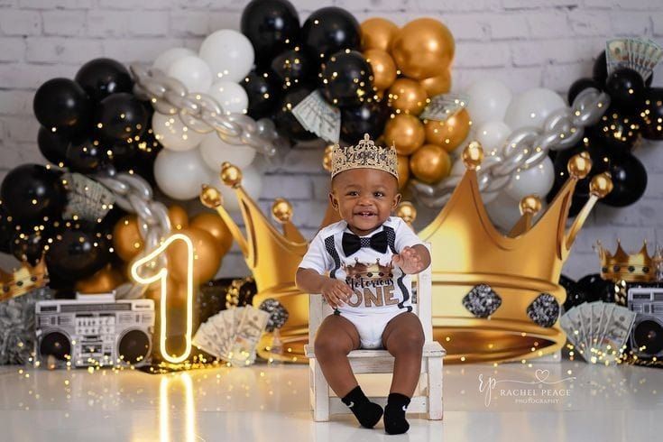 a baby wearing a crown sits on a chair in front of balloons