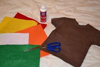 a pair of scissors and t - shirt sitting on top of sheets of fabric next to a bottle of glue